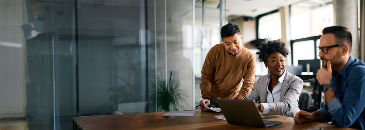 Trois professionnels diversifiés collaborent dans un bureau moderne, discutant de travail autour d’un ordinateur portable.